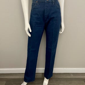 May include: Dark blue denim jeans with a classic straight leg fit. The jeans have a button and zipper closure, and five-pocket styling. The jeans are displayed on a mannequin.