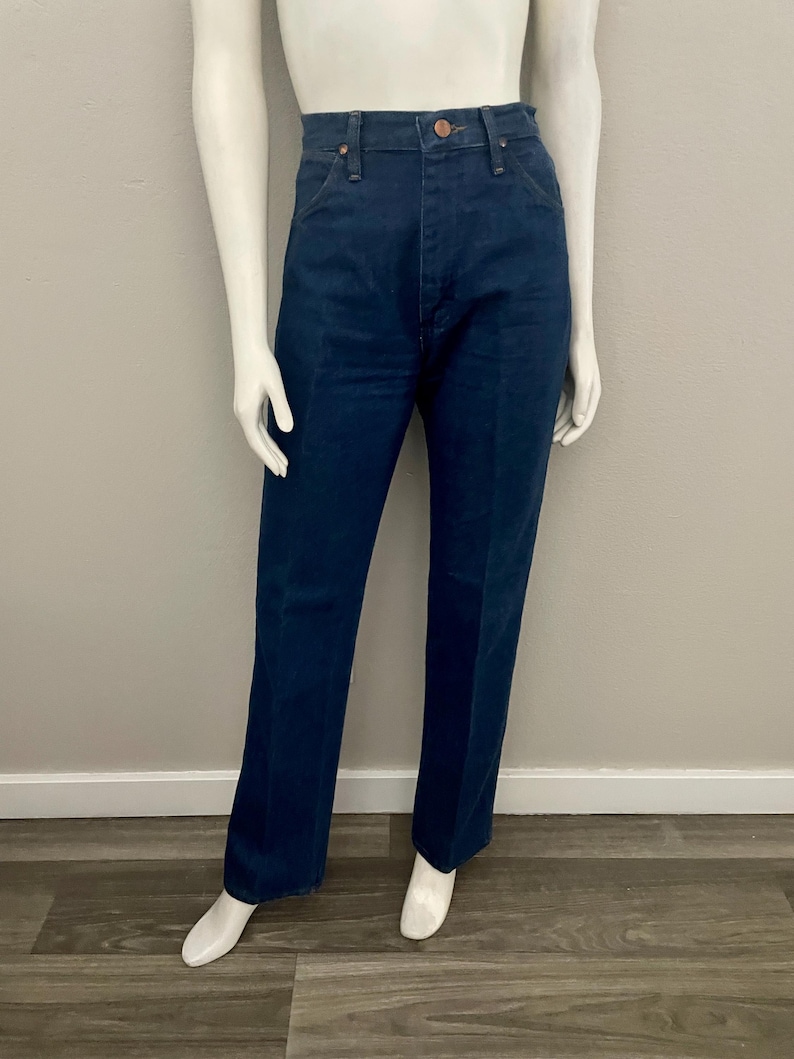 May include: Dark blue denim jeans with a classic straight leg fit. The jeans have a button and zipper closure, and five-pocket styling. The jeans are displayed on a mannequin.