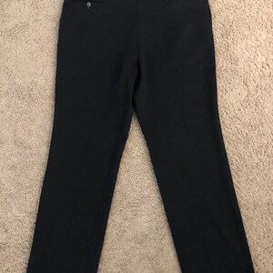 May include: Black dress pants with a buttoned back pocket and a small button detail. The pants are made of a smooth, dark fabric and have a classic, straight-leg design. The pants are laid flat on a neutral-colored surface.