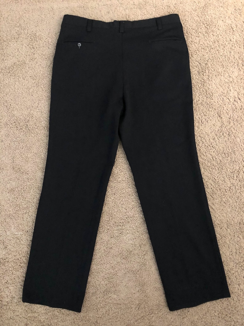 May include: Black dress pants with a buttoned back pocket and a small button detail. The pants are made of a smooth, dark fabric and have a classic, straight-leg design. The pants are laid flat on a neutral-colored surface.