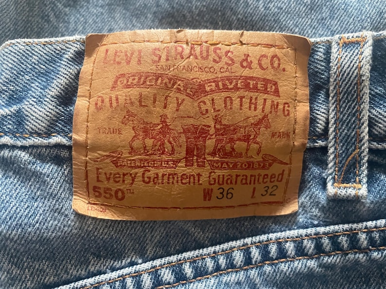 May include: Close-up of a light blue denim jeans with a brown leather label. The label reads "LEVI STRAUSS & CO. ORIGINAL RIVETED QUALITY CLOTHING" with "550" and measurements W36 L32.