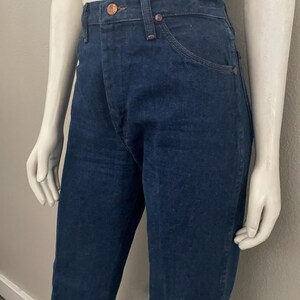 May include: Dark blue denim jeans with a classic five-pocket design. The jeans have copper-colored rivets and a button closure. The fabric appears to be a medium weight denim, suitable for everyday wear. The jeans are displayed on a mannequin.