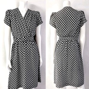 May include: A black and white patterned dress with a wrap-style waist and short sleeves. The dress features a V-neckline and a knee-length skirt. The fabric has a repeating pattern of small, elongated shapes.