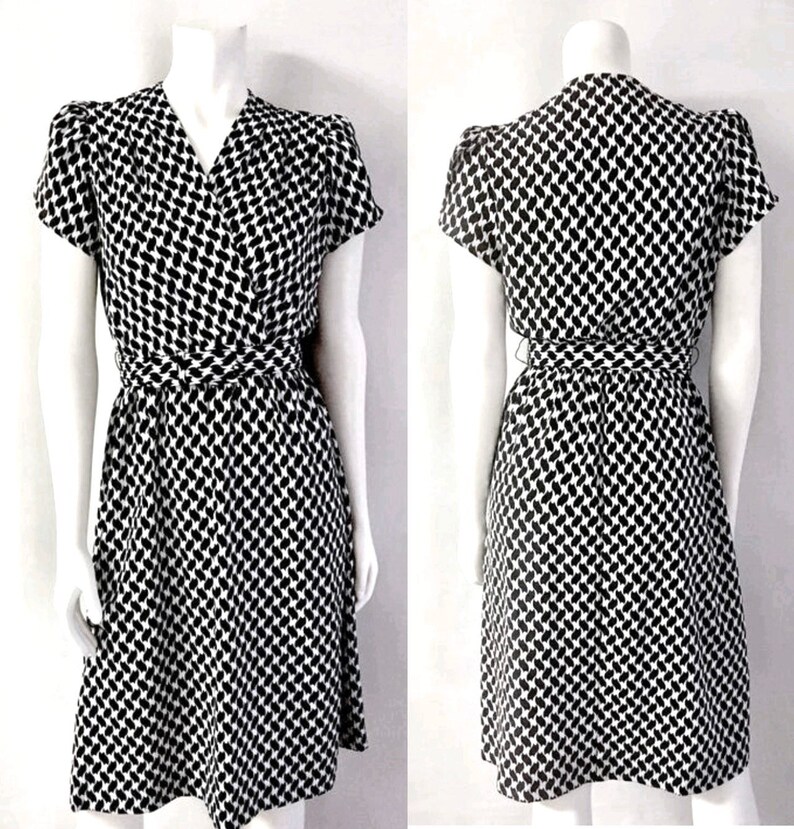 May include: A black and white patterned dress with a wrap-style waist and short sleeves. The dress features a V-neckline and a knee-length skirt. The fabric has a repeating pattern of small, elongated shapes.