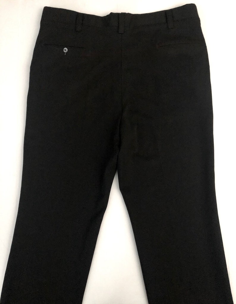 May include: Black dress pants with a buttoned back pocket and a buttoned closure. The pants are made of a smooth, solid fabric and have a classic, tailored design. The pants are suitable for formal or business attire.