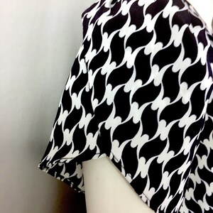 May include: A black and white patterned top with a repeating wave design. The fabric is draped over a mannequin, showcasing the sleeve and shoulder detail. The pattern is a bold, graphic design.