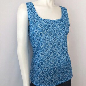 May include: A sleeveless tank top in shades of blue, featuring a floral pattern. The top has a scoop neckline and wide straps. The fabric appears lightweight and suitable for warm weather.