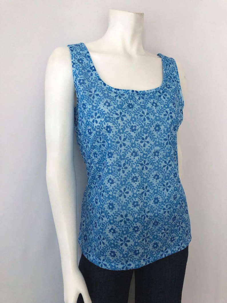 May include: A sleeveless tank top in shades of blue, featuring a floral pattern. The top has a scoop neckline and wide straps. The fabric appears lightweight and suitable for warm weather.