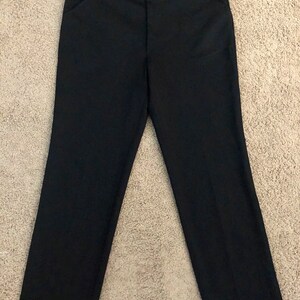 May include: Black dress pants with a straight leg design. The pants have a classic five-pocket style and a button and zipper closure. The pants are made of a solid black fabric.