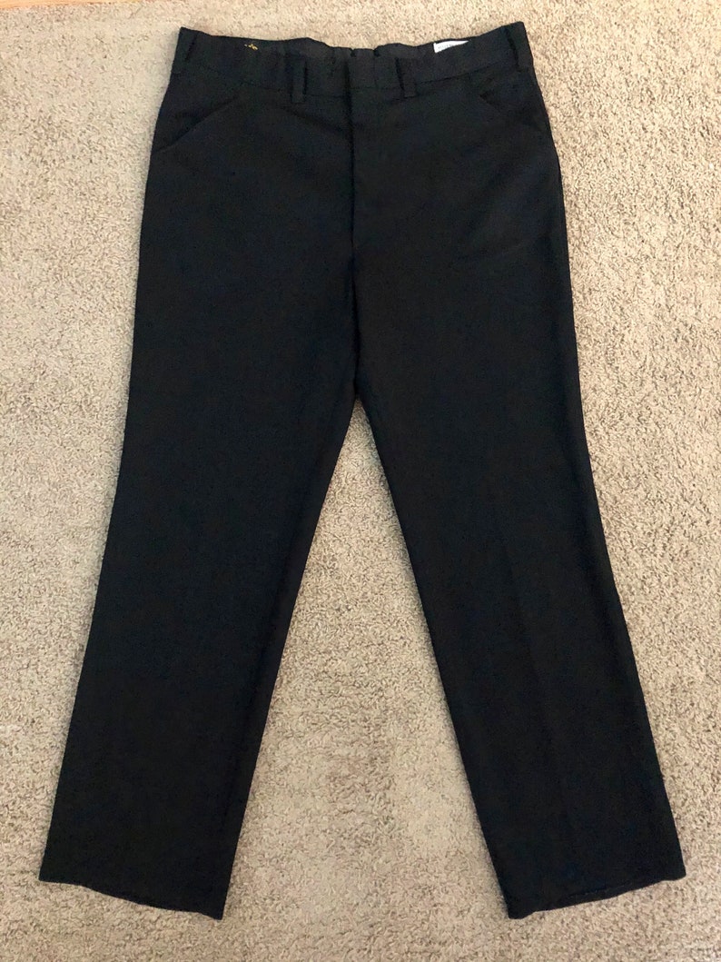 May include: Black dress pants with a straight leg design. The pants have a classic five-pocket style and a button and zipper closure. The pants are made of a solid black fabric.