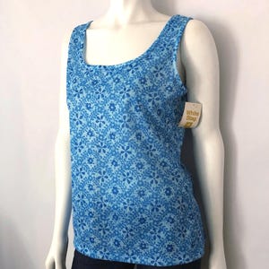 May include: A blue tank top with a floral pattern. The top has a scoop neckline and wide straps. The tag reads "White Stag". The tank top is displayed on a mannequin.