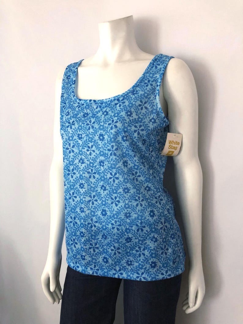 May include: A blue tank top with a floral pattern. The top has a scoop neckline and wide straps. The tag reads "White Stag". The tank top is displayed on a mannequin.