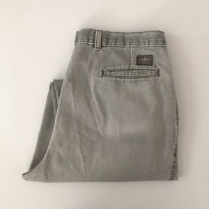 May include: Light grey denim trousers with a folded design. The trousers have a small rectangular patch on the back pocket. The trousers are folded neatly on a white surface.