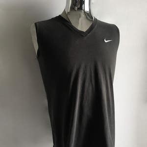 Puede incluir: Camiseta sin mangas gris oscuro con cuello en V y logotipo blanco de Nike en el pecho. La camiseta se muestra en un maniqu&iacute;. La tela parece suave y ligeramente desgastada, lo que sugiere un estilo informal. El aspecto general es sencillo y deportivo.