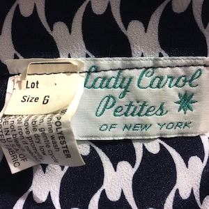 May include: Close-up of a vintage clothing label from "Lady Carol Petites of New York." The label is white with teal lettering and a starburst design. The fabric has a navy and white abstract pattern. A size 6 tag is attached.