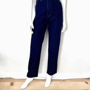 K&ouml;nnte beinhalten: Dunkelblaue Jeanshose mit hohem Bund und geradem Bein. Die Hose hat einen Knopf- und Rei&szlig;verschluss sowie wei&szlig;e Steppn&auml;hte. Pr&auml;sentiert auf einer Schaufensterpuppe.