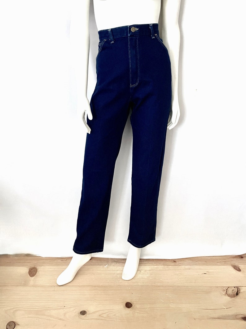 K&ouml;nnte beinhalten: Dunkelblaue Jeanshose mit hohem Bund und geradem Bein. Die Hose hat einen Knopf- und Rei&szlig;verschluss sowie wei&szlig;e Steppn&auml;hte. Pr&auml;sentiert auf einer Schaufensterpuppe.
