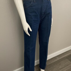 May include: Dark blue denim jeans with a classic straight leg fit. The jeans have a high waist, five-pocket design, and a button and zipper closure. The jeans are displayed on a mannequin.