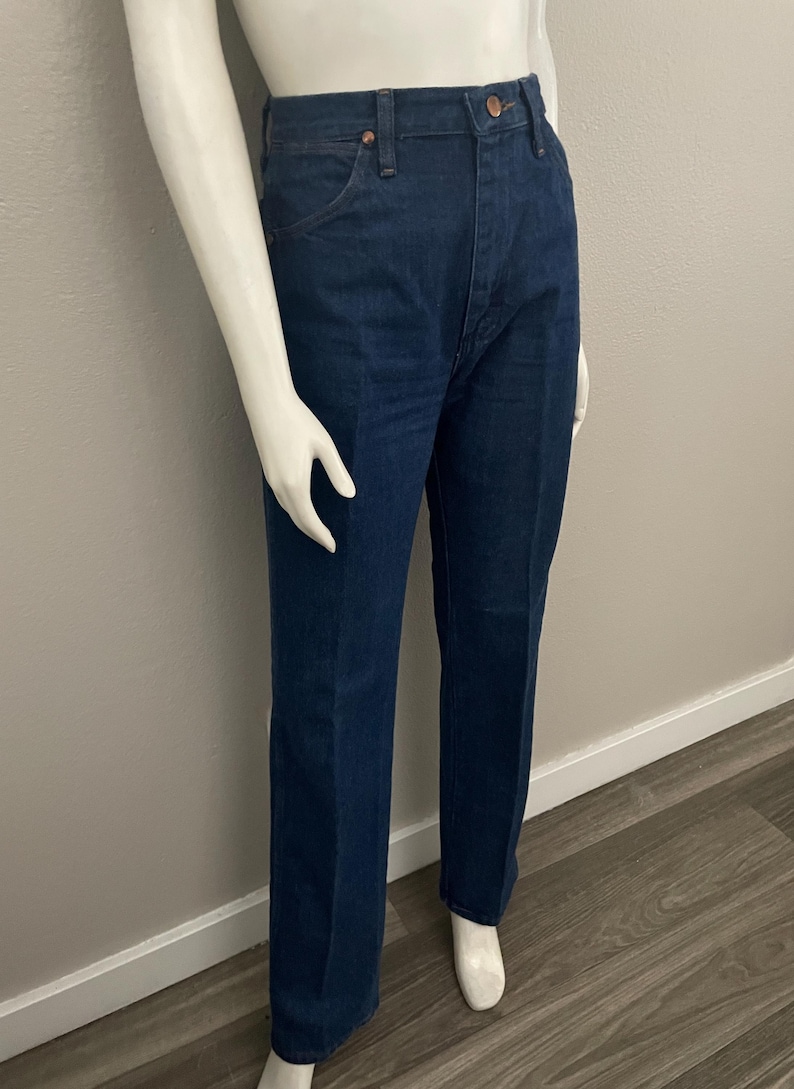 May include: Dark blue denim jeans with a classic straight leg fit. The jeans have a high waist, five-pocket design, and a button and zipper closure. The jeans are displayed on a mannequin.