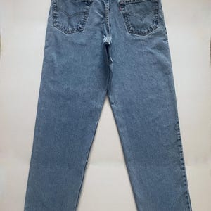 May include: Light blue denim jeans with a classic five-pocket design. The jeans feature a straight leg cut and a leather patch on the back waistband. The back pockets have a signature stitch detail.