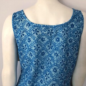 May include: Sleeveless blue dress with a floral pattern. The dress features a scoop neckline and is made of a lightweight fabric. The floral design includes various shades of blue, creating a visually appealing garment.