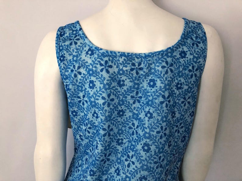 May include: Sleeveless blue dress with a floral pattern. The dress features a scoop neckline and is made of a lightweight fabric. The floral design includes various shades of blue, creating a visually appealing garment.