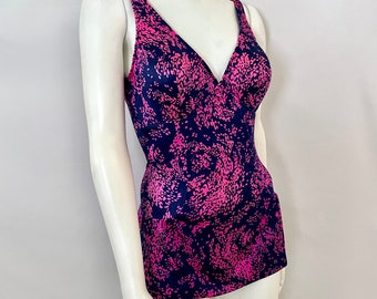 Pode incluir: Top de fato de banho com padrão azul marinho e rosa com decote em V. O top apresenta um padrão abstrato rosa vibrante sobre um fundo azul marinho. As alças são largas e o tecido parece liso, possivelmente sedoso. Exibido em um manequim.