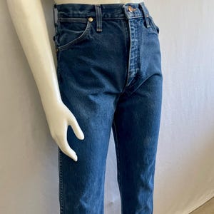 May include: Dark blue denim jeans with a classic straight-leg fit. The jeans feature a button and zipper closure, along with classic five-pocket styling. The jeans are displayed on a mannequin.