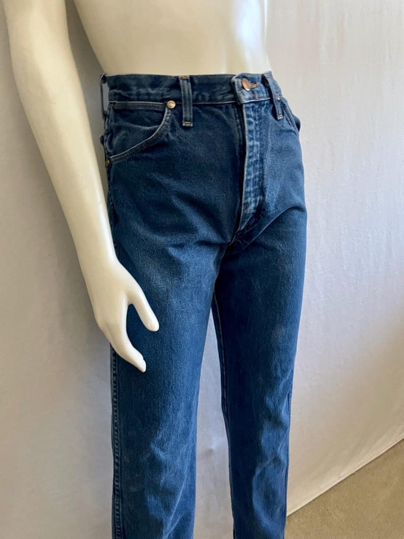 May include: Dark blue denim jeans with a classic straight-leg fit. The jeans feature a button and zipper closure, along with classic five-pocket styling. The jeans are displayed on a mannequin.