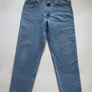 May include: Light blue denim jeans with a classic five-pocket design. The jeans have a straight leg cut and a button and zipper closure. The denim has a faded appearance, suggesting a worn-in look. The jeans are laid flat on a white surface.