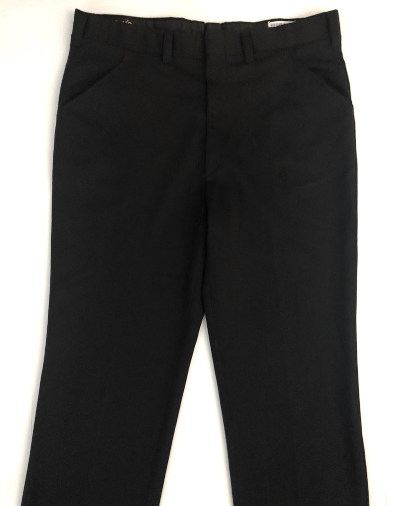 May include: A pair of black dress pants with a classic, straight-leg design. The pants feature front pockets, belt loops, and a button and zipper closure. The fabric appears to be a smooth, solid black, suitable for formal or professional wear.