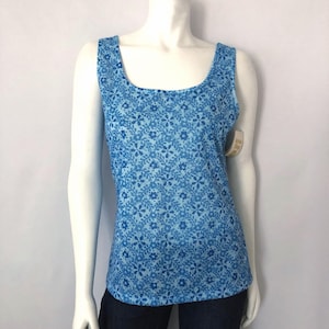 May include: A blue tank top with a floral pattern. The top has a square neckline and wide straps. The floral pattern is a lighter shade of blue against a darker blue background. The tank top is displayed on a mannequin.
