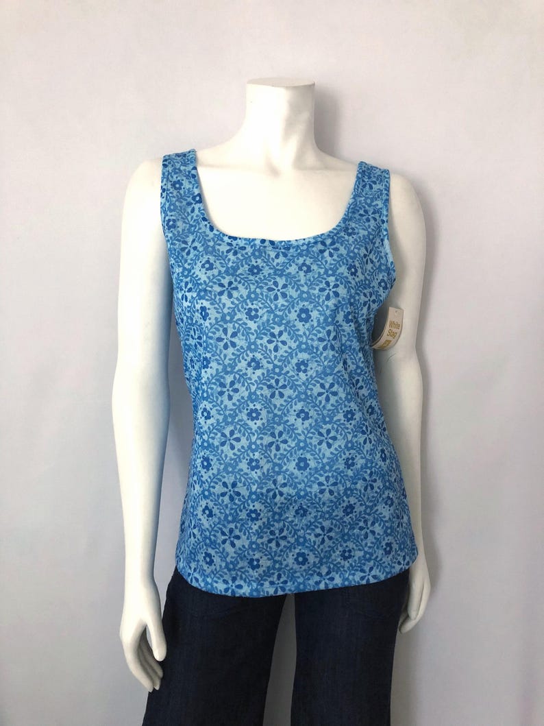 May include: A blue tank top with a floral pattern. The top has a square neckline and wide straps. The floral pattern is a lighter shade of blue against a darker blue background. The tank top is displayed on a mannequin.