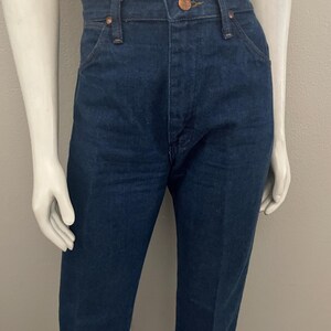 May include: Dark blue denim jeans with a classic five-pocket design. The jeans have a button and zipper closure, belt loops, and copper-colored rivets. The straight-leg style is displayed on a mannequin.