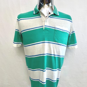 May include: A short-sleeved polo shirt with horizontal stripes in white, green, and blue. The shirt has a collar, a pocket on the chest, and is displayed on a mannequin. The shirt's sleeves and collar are white.