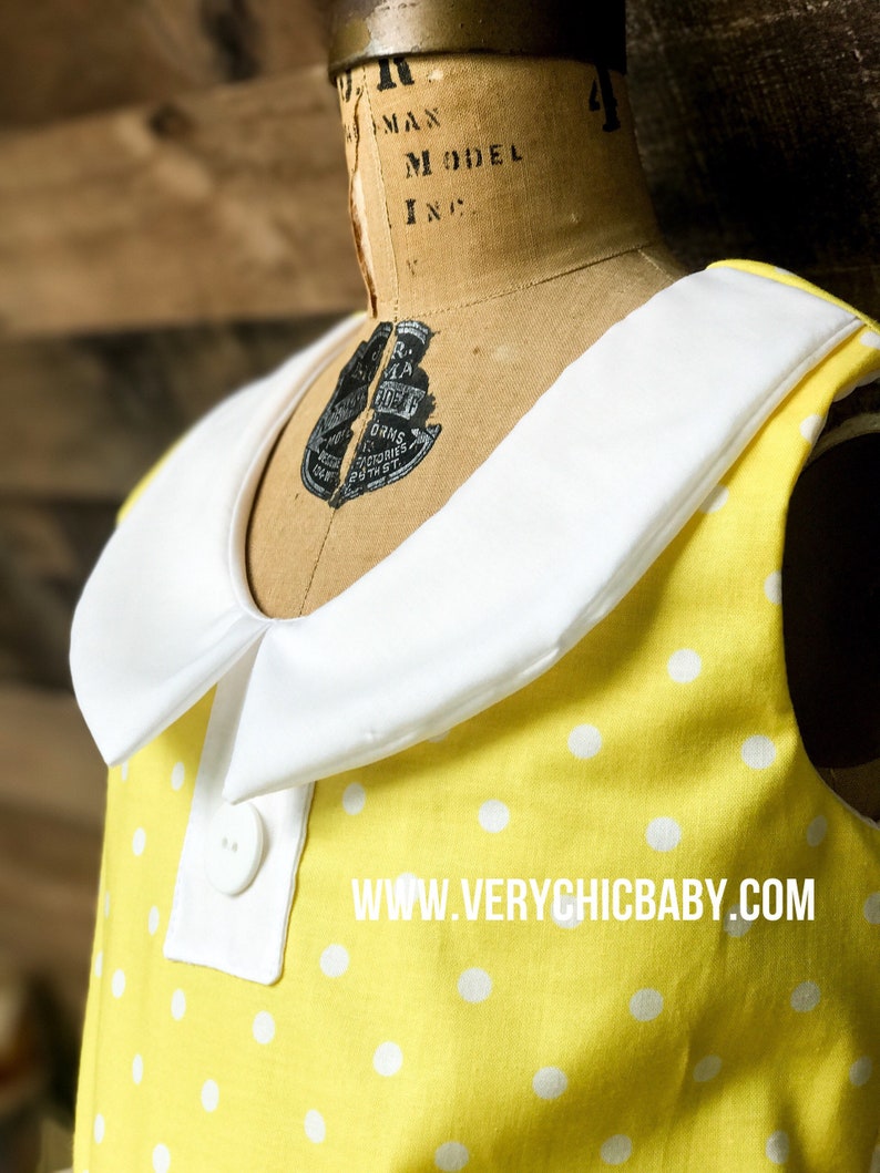 May include: A yellow sleeveless dress with white polka dots and a white Peter Pan collar. The dress has two white buttons on the front. The dress has the text "www.verychicbaby.com" printed on the front.