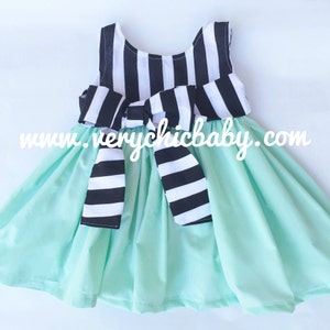 May include: A sleeveless dress with a black and white striped bodice and a mint green skirt. The bodice has a large black and white striped bow at the waist. The dress has a website address printed on the front: www.verychicbaby.com