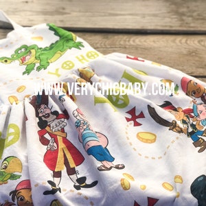 Può includere: Un abito bianco senza maniche a tema Peter Pan. L'abito presenta una varietà di personaggi dello show, tra cui Capitan Uncino, Peter Pan e il coccodrilo. L'abito ha anche monete d'oro e una mappa stampata su di esso. Il testo "Yo Ho" è stampato sull'abito.