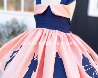 Può includere: Un vestito rosa e blu navy con un colletto alla Peter Pan e una gonna con silhouette di personaggi di Star Wars. La gonna ha una silhouette blu navy di Darth Vader, una silhouette blu navy della principessa Leia, una silhouette blu navy di Han Solo e una silhouette blu navy del Millennium Falcon. Il testo "www.verychicbaby.com" è stampato sulla gonna.
