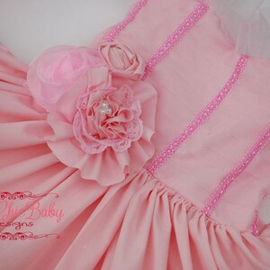 May include: A pink dress with a ruffled flower embellishment and pink lace trim. The dress has a tulle overlay and a satin bodice.