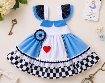 Könnte beinhalten: Ein blau-weißes Kleid mit einer weißen Schürzenblende, einer roten Herzapplikation, einem schwarz-weiß karierten Saum, dunkelblauen, gepunkteten Flügelärmeln und einer passenden blauen Rosette. Das Kleid enthält ein weißes Etikett mit einer Illustration.