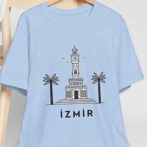 May include: Light blue t-shirt with a black and white illustration of a clock tower with palm trees and the text "İZMİR" on the front.