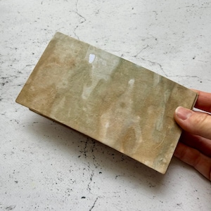 May include: A rectangular paper notepad with a mottled, tea-stained appearance featuring shades of tan, beige, and muted green. The surface has a textured, organic look with subtle variations in color density across the entire rectangular sheet.