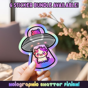May include: A holographic sticker featuring a cartoon cow being beamed up by a UFO, with a small bear in the UFO. The sticker has a colorful, iridescent border and the text "6 STICKER BUNDLE AVAILABLE!" and "holographic shatter finish!"