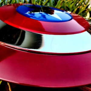May include: A red, white and blue Captain America shield with a silver metal rim. The shield is made of a durable material and has a glossy finish.