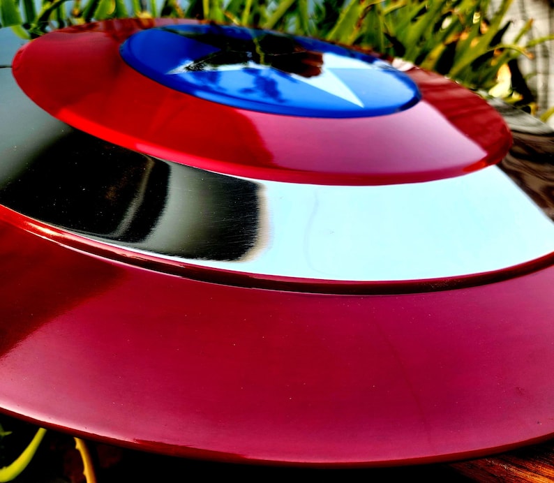 May include: A red, white and blue Captain America shield with a silver metal rim. The shield is made of a durable material and has a glossy finish.