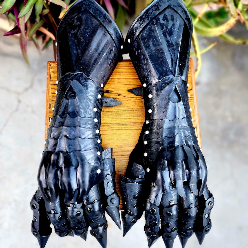May include: A pair of black metal gauntlets with articulated fingers and spiked knuckles. The gauntlets have a textured surface and are decorated with rivets.