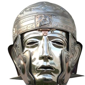 May include: A polished silver Roman helmet with a face mask design. The helmet features intricate embossed patterns and a hinged brow guard. The face mask has detailed facial features, including a nose, mouth, and eyes. The helmet is a historical replica.