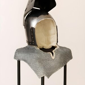 May include: A medieval helmet with a hinged visor and a chainmail neck guard. The helmet is black with a padded interior. The chainmail is silver. The helmet is displayed on a black stand.