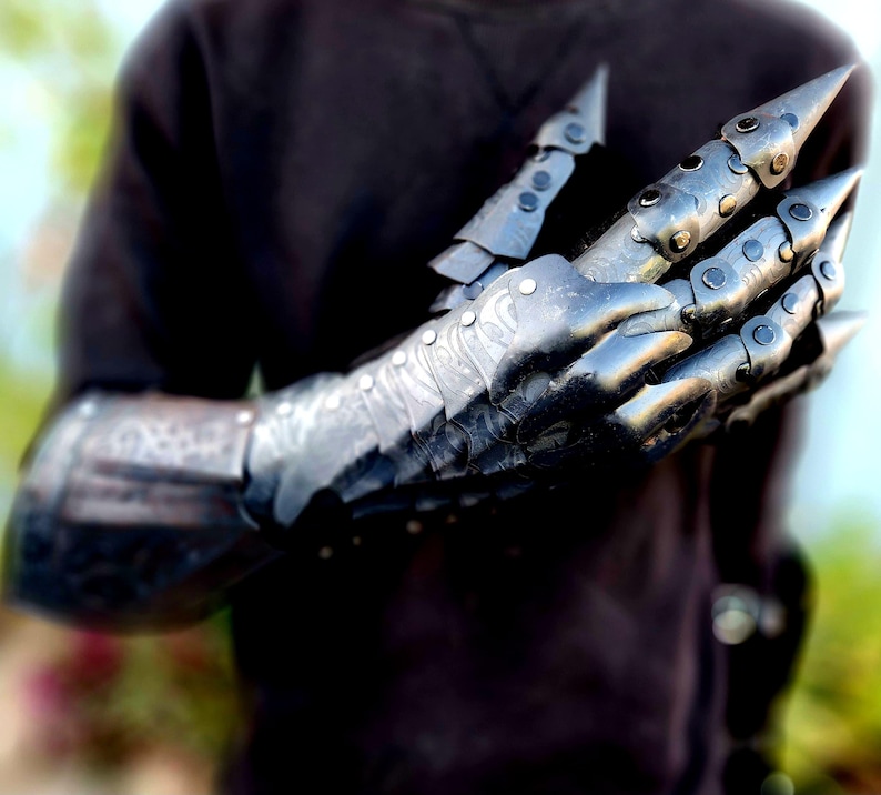 May include: A black metal gauntlet with articulated fingers and sharp claws. The gauntlet is worn on a person's arm, and the fingers are curled into a fist.